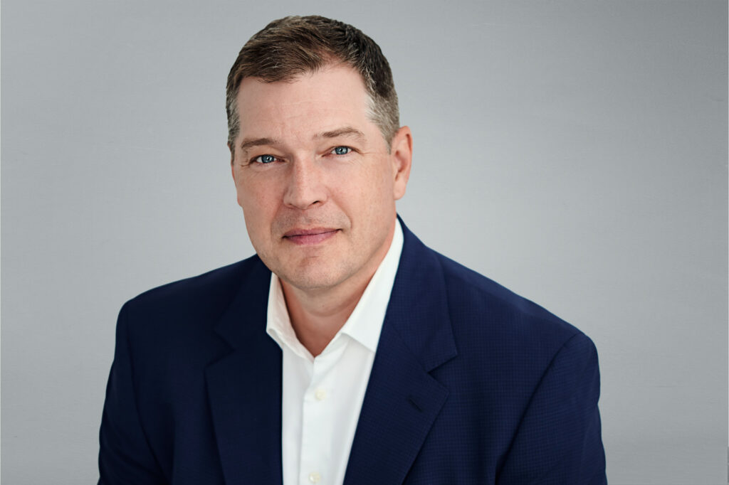 Professor de Beer in a formal, seated pose wearing a navy suit with a white dress shirt.